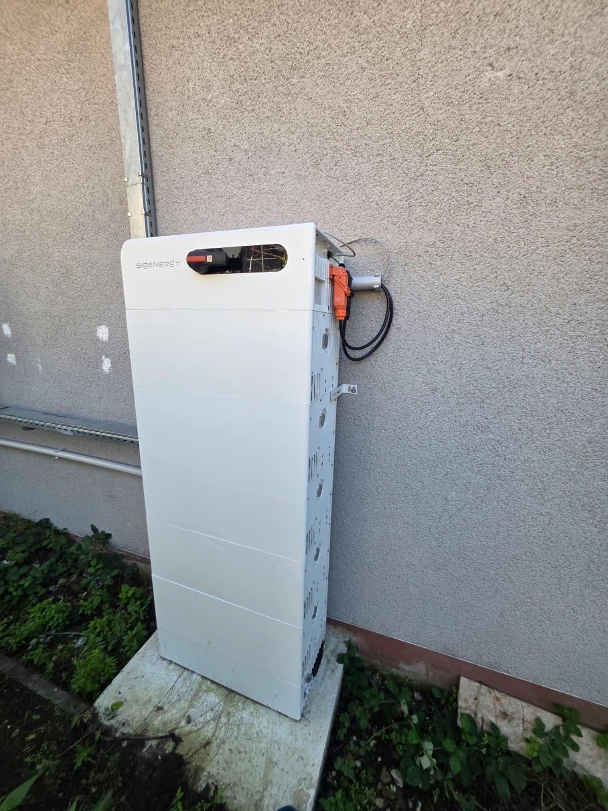 Speicherturm schräg von der Seite: an der Schmalseite ein orangefarbener Stecker, schwarze Leitungen und ein Haltewinkel zur Wand