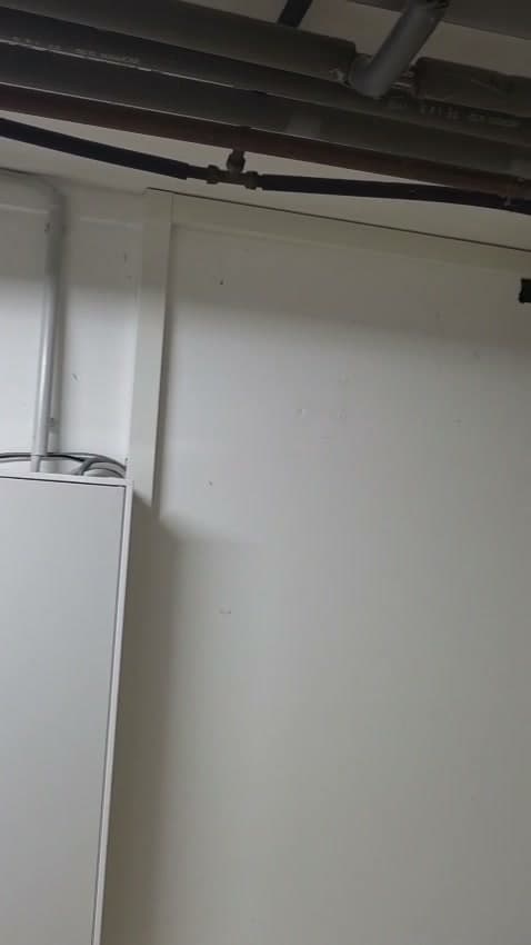 Obere Ecke des Hausanschlussraums: Vom Zählerschrank führen ein weißer Kabelkanal und ein graues Installationsrohr hinauf zur Decke