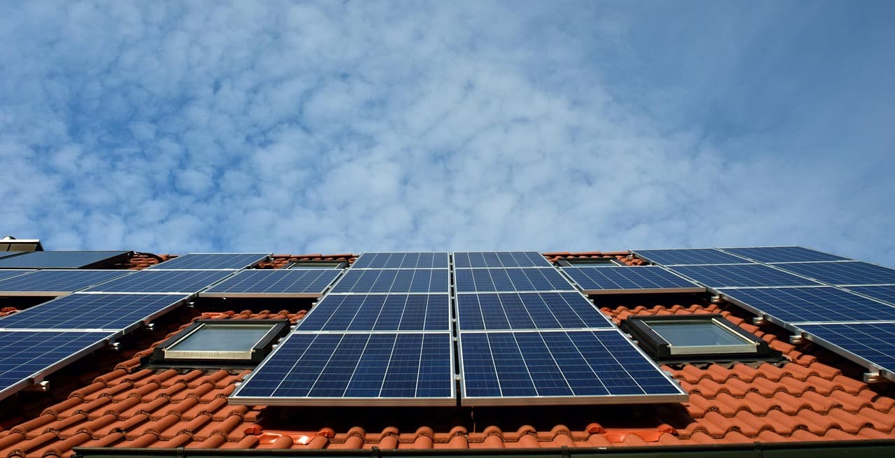 Photovoltaik-Module auf einem roten Ziegeldach mit Dachfenstern unter blauem Himmel mit Wolken