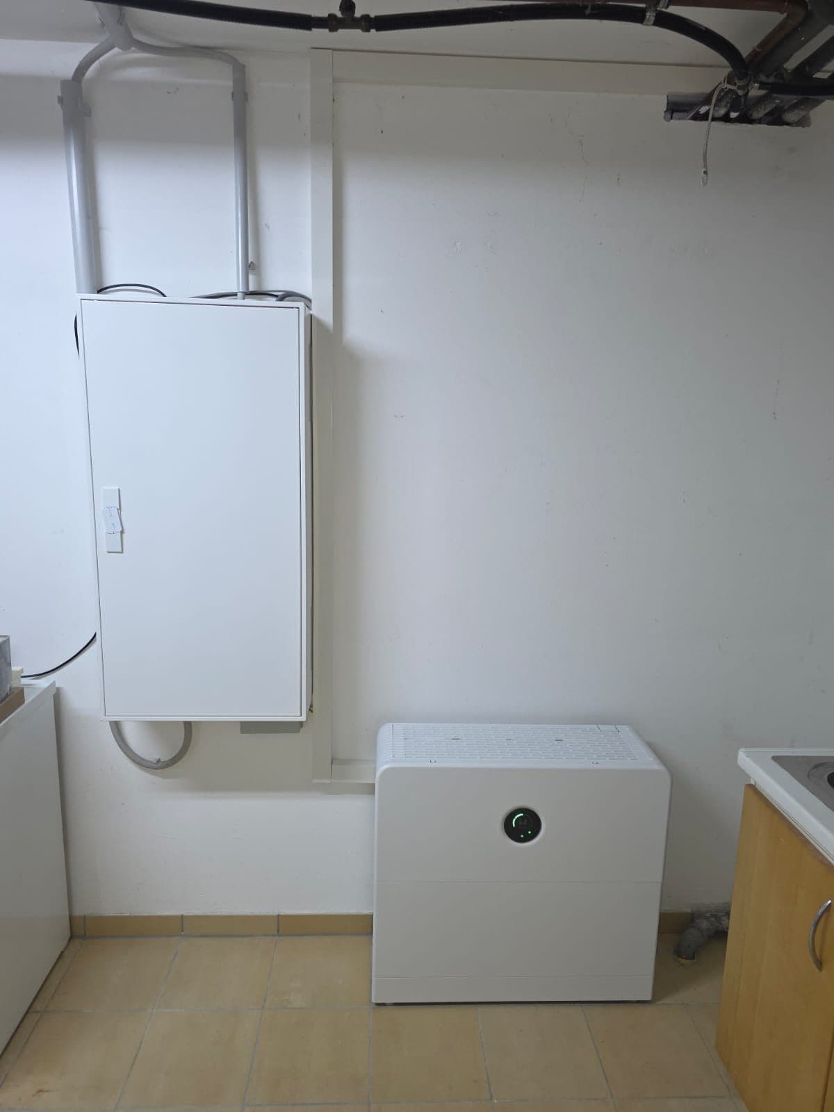Neuer weißer Zählerschrank an der Wand, schräg darunter der GoodWe ESA mit leuchtender Anzeige, im Raum ein gefliester Boden